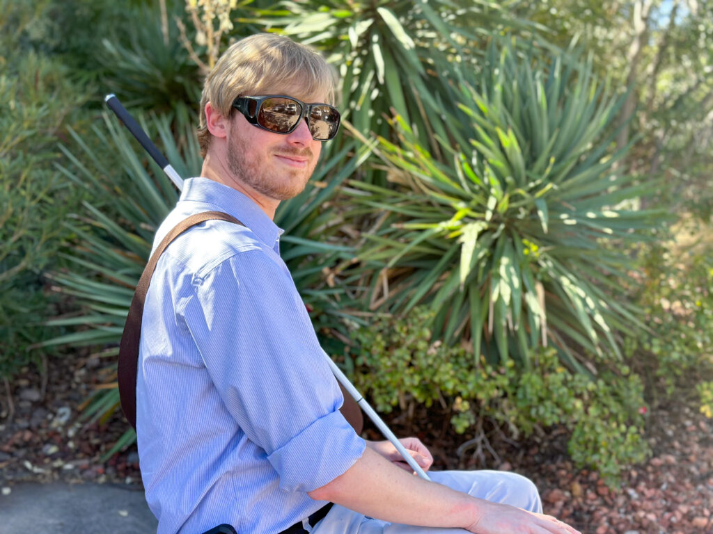 Tyson in sunglasses outdoors with greenery.