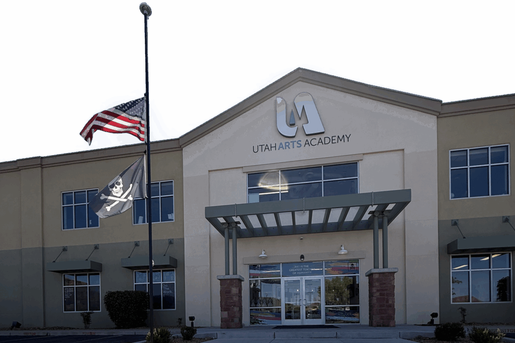 Front exterior of Utah Arts Academy building with entrance, signage, and flags displayed outside.